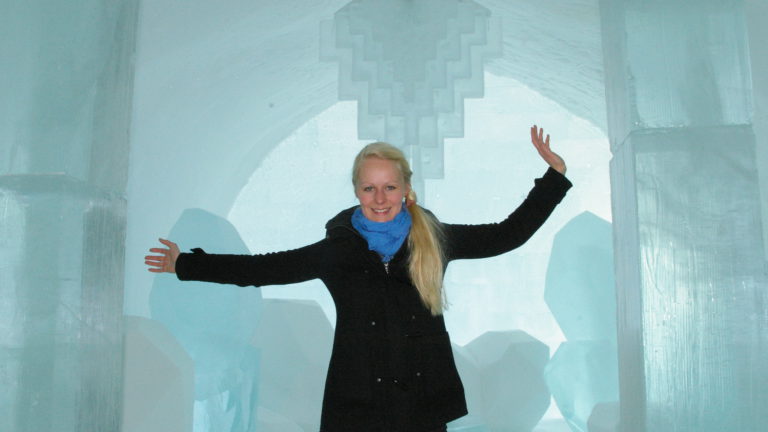 Birte steht im Eishotel Jukkasjärvi in Schweden. Im Hintergrund sieht man einen Kronleuchter aus Eis.